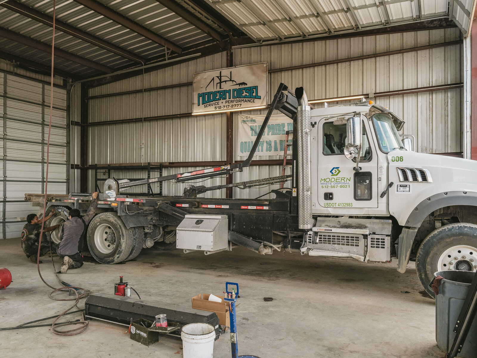 Roll-off truck in a Modern Diesel bay with two technicians at the rear axle