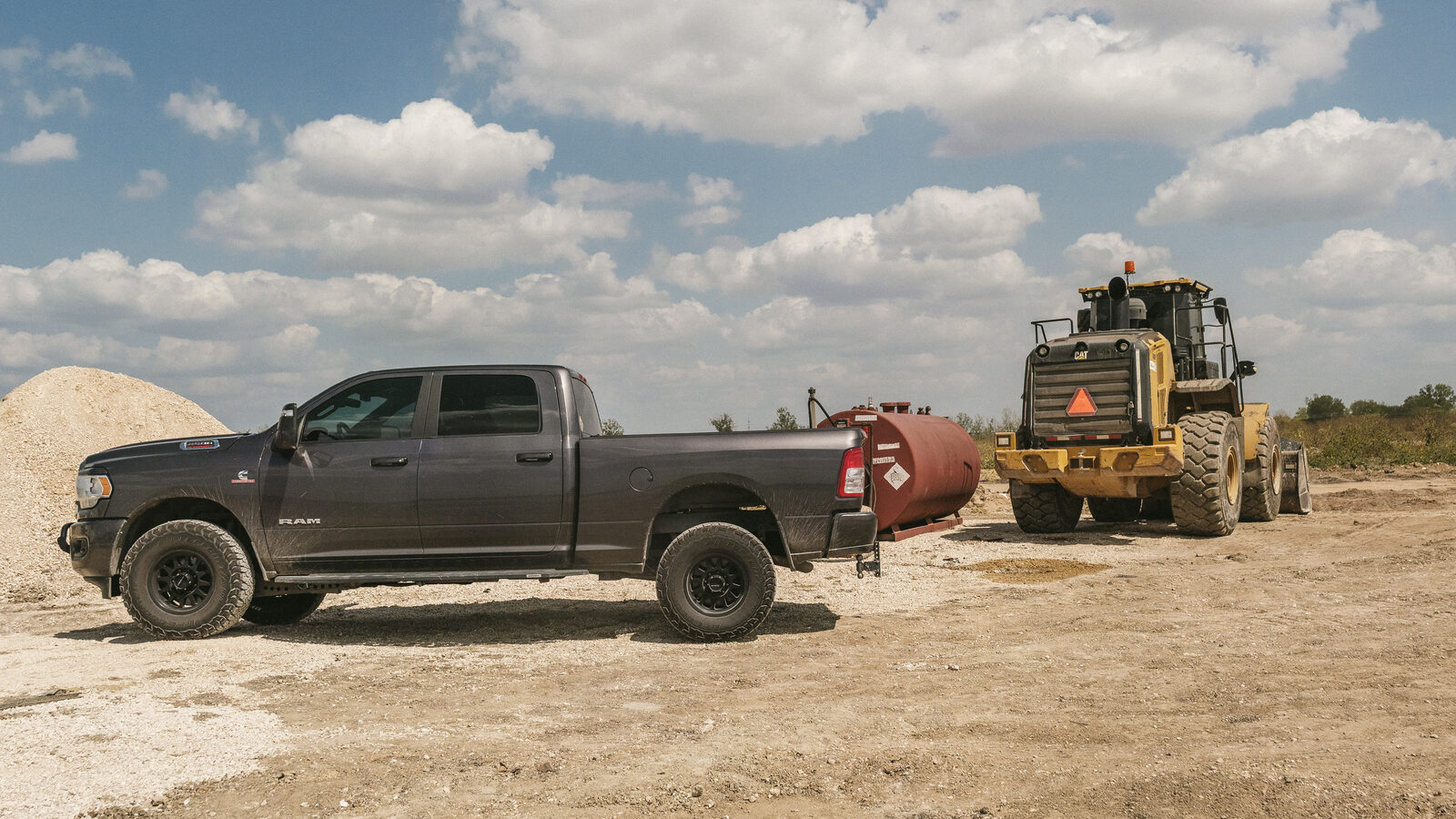 Ram 2500 with a bed-mounted transfer tank parked on a job site next to a Cat wheel loader