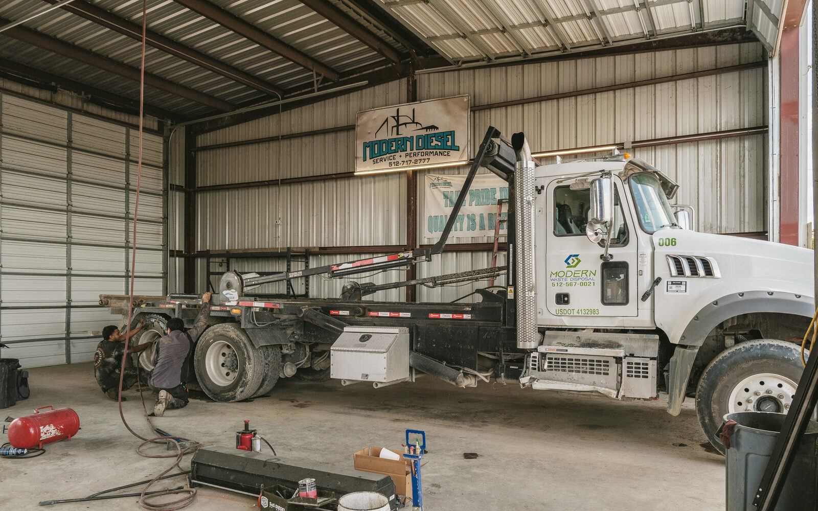 Roll-off truck in a Modern Diesel bay with two technicians at the rear axle